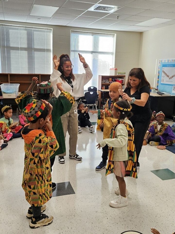 During a school social work internship in fall 2024, University of North Carolina at Charlotte MSW student Mariam Sheriff (in white sweater with raised hands) helps first-graders participate in a traditional African dance at Charlotte’s Parkside Elementary School